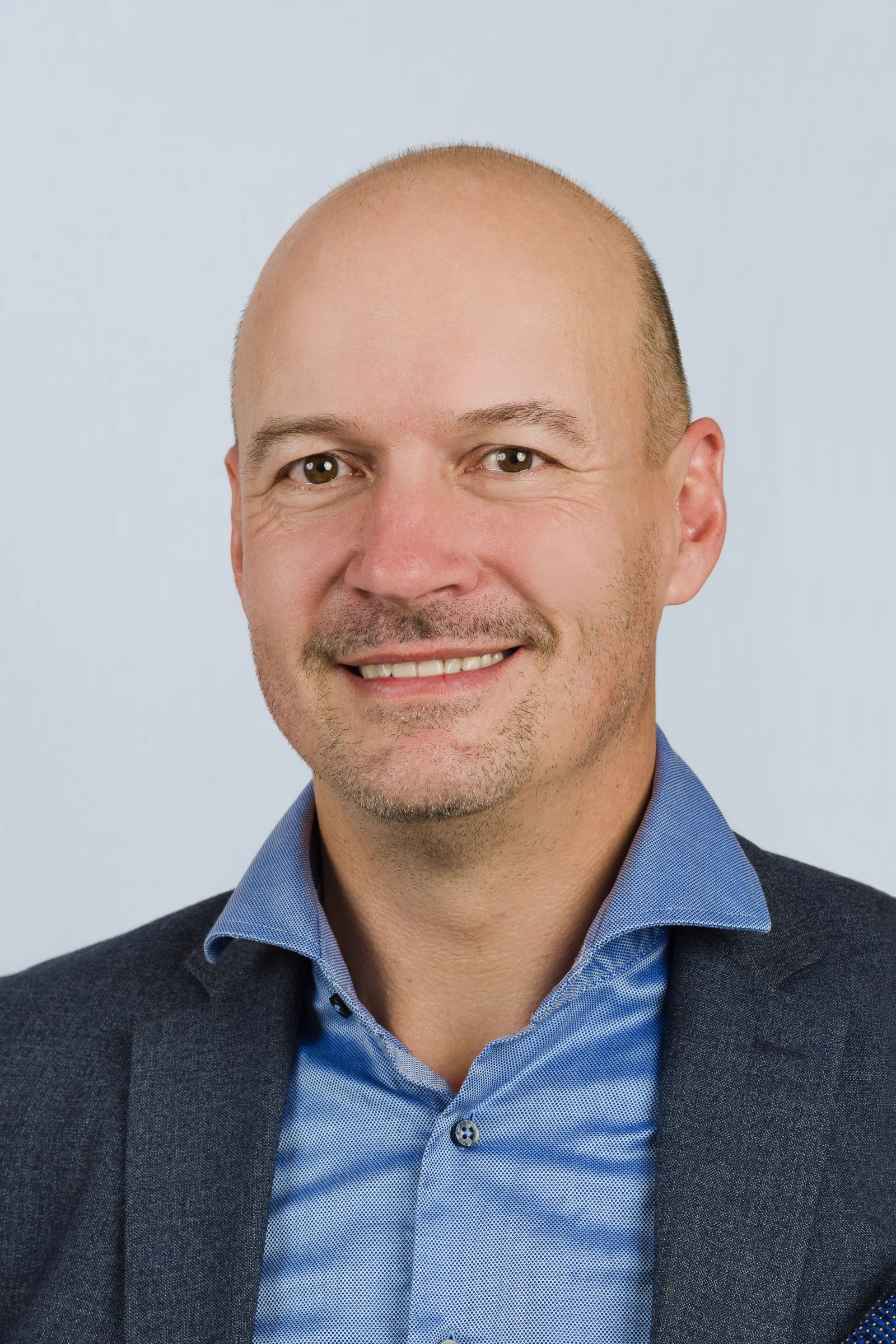 Porträt eines Mannes mit Glatze, der einen blauen Anzug und ein Hemd trägt.