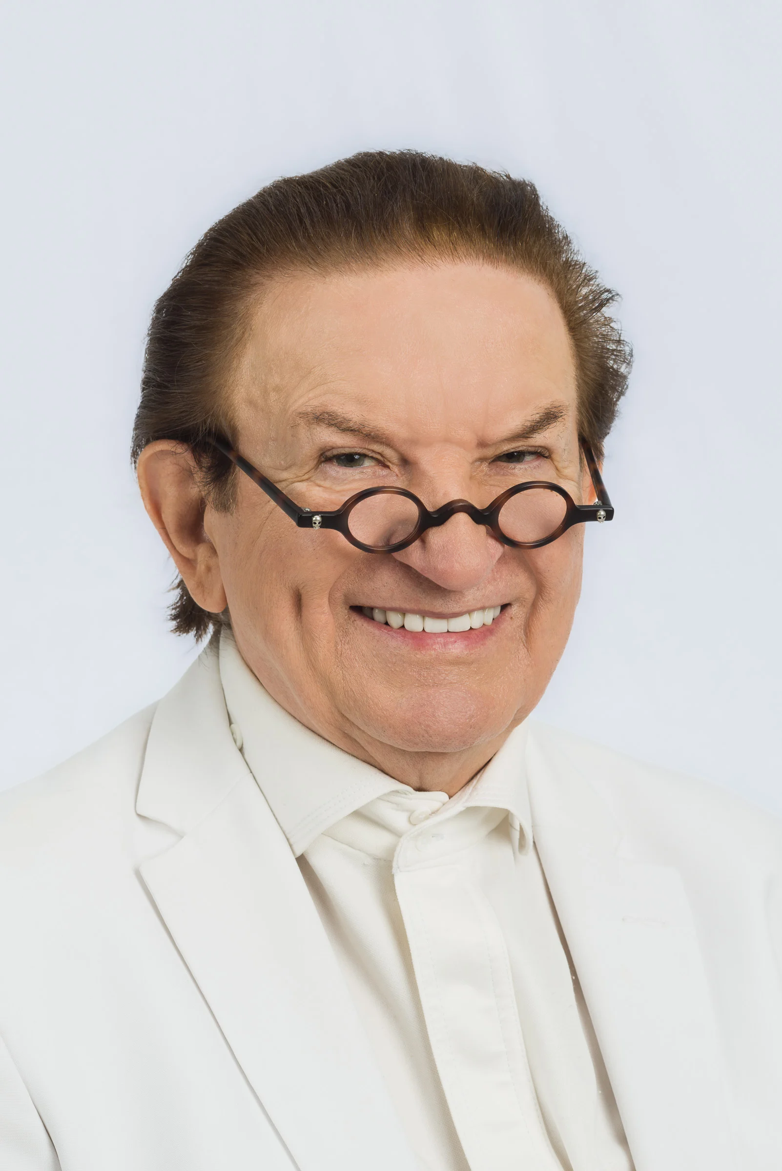 Lächelnder Mann mit Brille und weißem Anzug, der in die Kamera schaut.